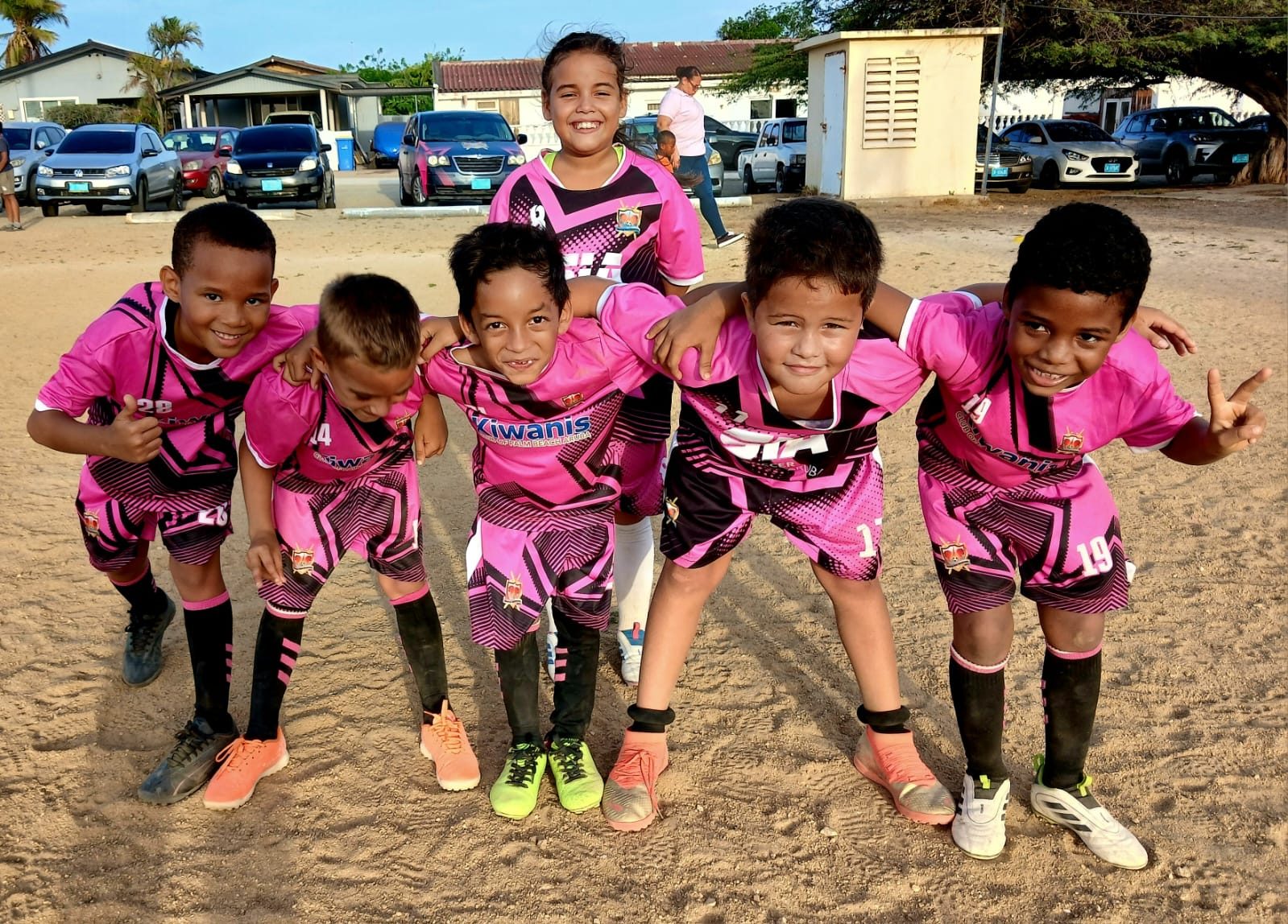 RCS U7 players in their pink kit, arms around each other on the Savaneta ground